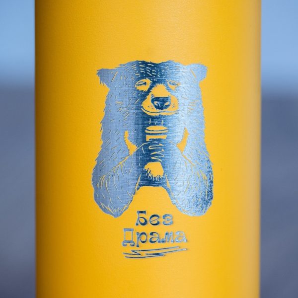Close-up of laser-engraved bear holding a cup with the text “Bez drama” on a yellow metal thermos.