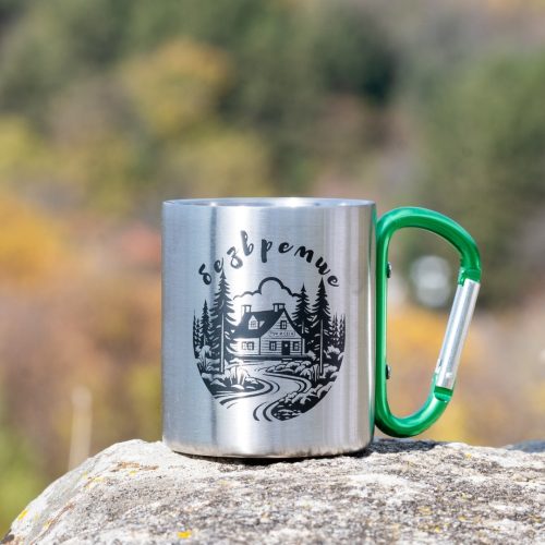 Stainless steel mug with printed forest cabin design and green carabiner handle.