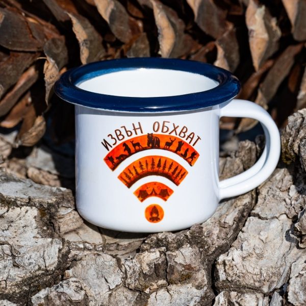 White enamel mug with blue rim and orange “Out of Range” Wi-Fi design made of forest animals and trees, placed outdoors on bark.