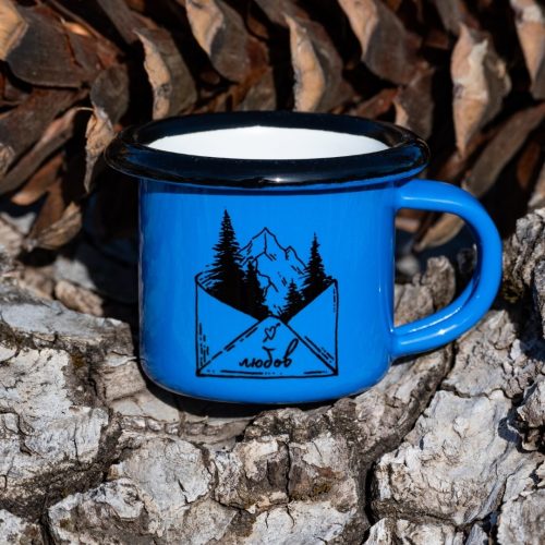 malko-kanche-za-kafe Small blue enamel mug with illustration of mountains and trees coming out of an envelope with the text “Love”, placed outdoors on bark.