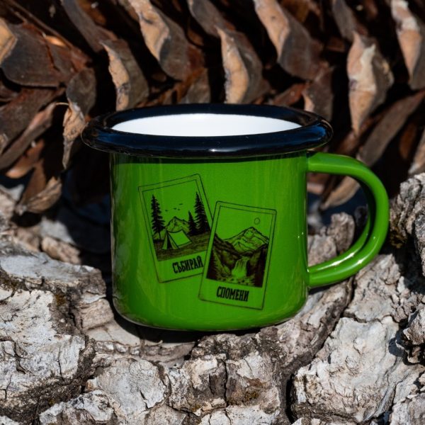 malko-zeleno-kanche-espresso Green enamel mug with black mountain and tent illustrations and the text “Collect Memories”, placed outdoors on bark.