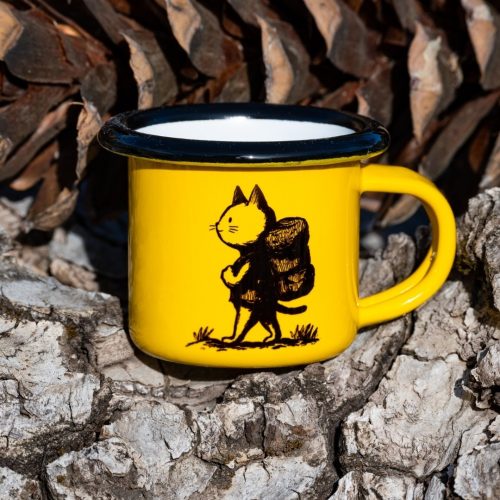 mini-metalna-chasha-espresso Yellow enamel mug with black illustration of a hiking cat carrying a backpack, placed outdoors on bark.
