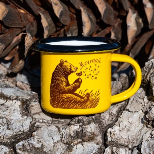 mini-zhylto-kanche Yellow enamel mug with black illustration of a bear holding a dandelion and the text “Dream”, placed outdoors on bark.