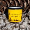 Yellow enamel mug with black illustration of a campfire, tent, and the text “Don’t burn the forest, light the fire in your soul”, placed outdoors on bark.