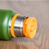 Close-up of the orange pouring cap and stainless steel neck of a green metal thermos.