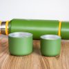 Two green metal cups from a camping thermos set placed on a wooden surface.